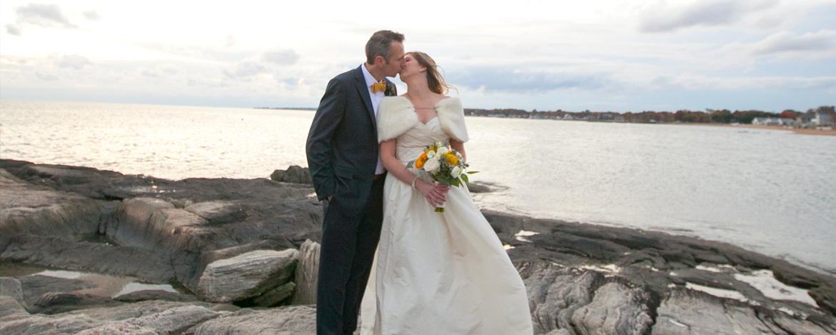 bride and groom kissing on the rocks at water's edge